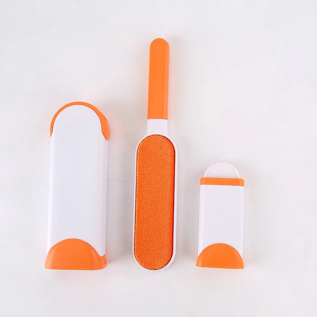 Orange pet hair remover brush with fabric pad beside its self-cleaning base and mini base