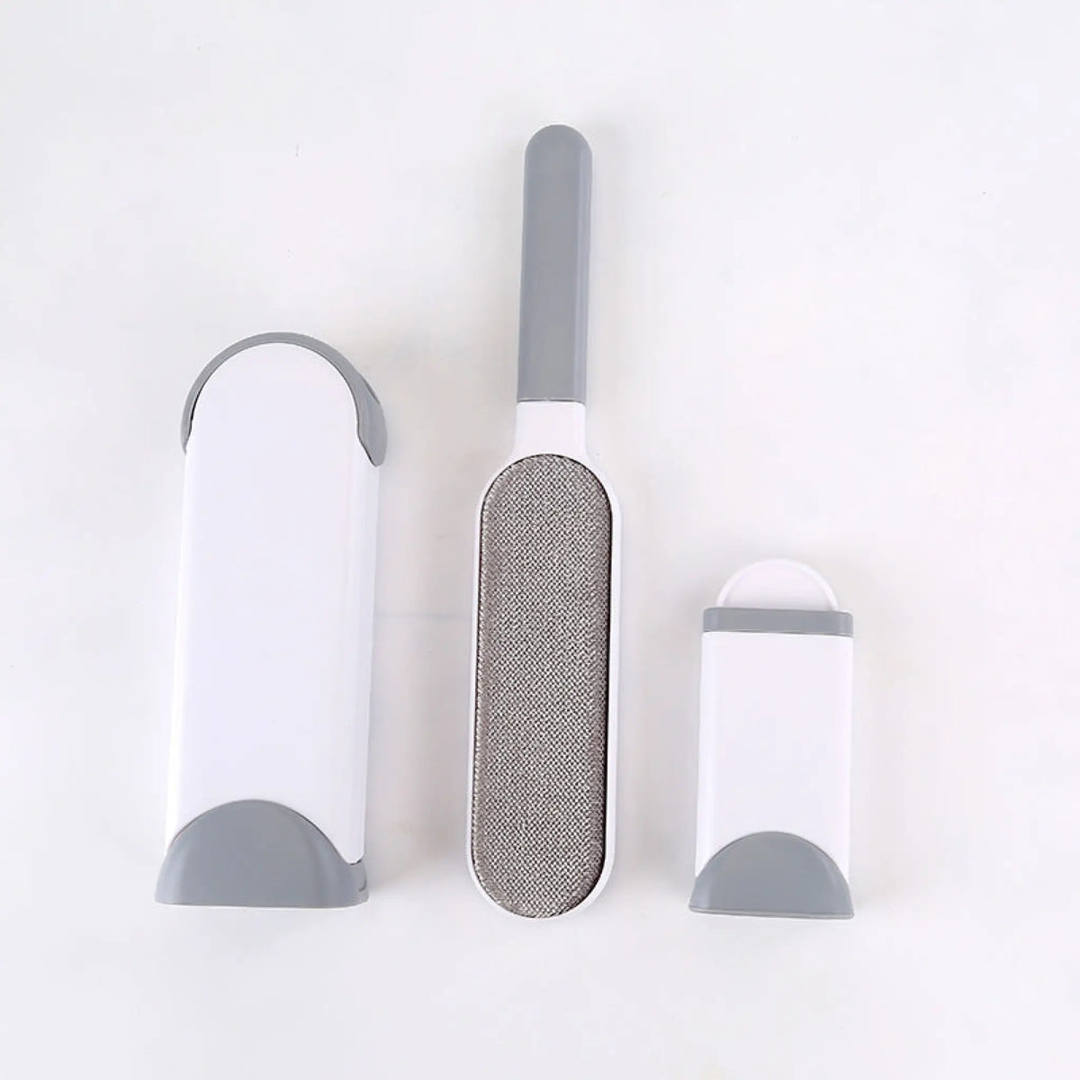 Gray pet hair remover brush with fabric pad beside its self-cleaning base and mini base