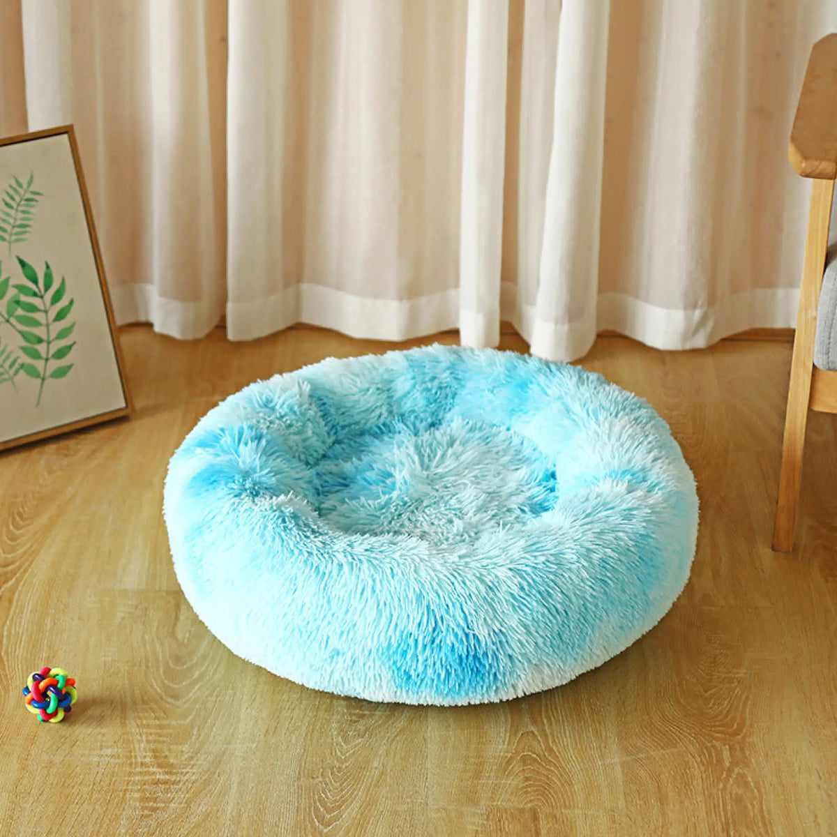 Tie-dye sky blue plush round pet bed on a wooden floor