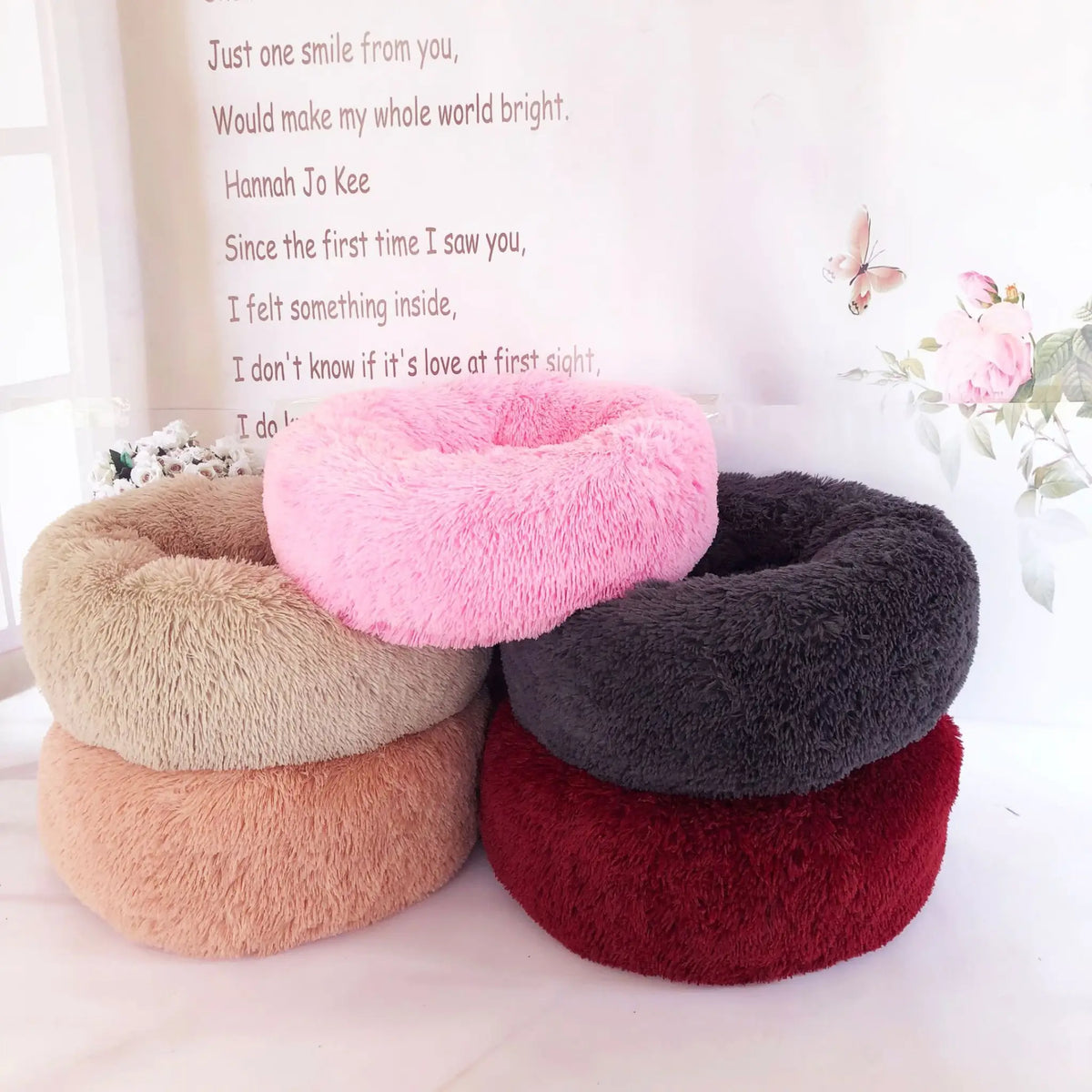 Stack of plush donut pet beds in pink, charcoal, burgundy, tan and peach